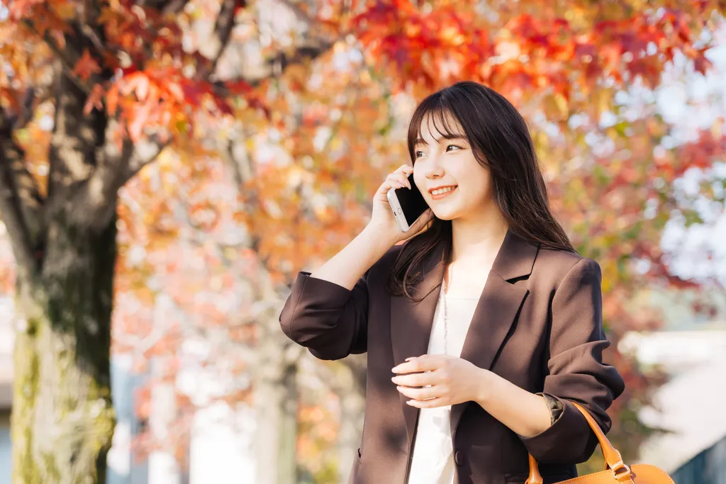 紅葉した木々を背景に笑顔で通話するビジネスウーマン